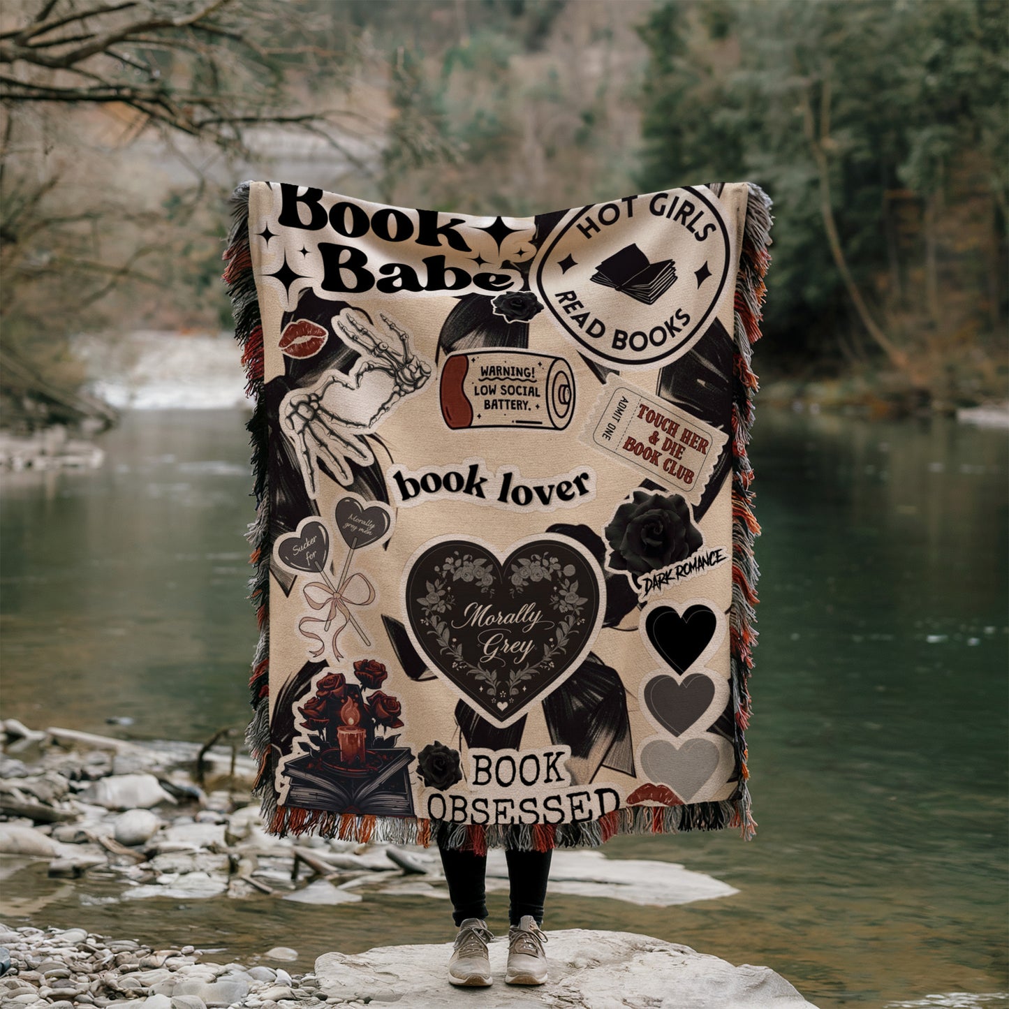 A person is standing on a rock, holding a blanket with various book-related designs and text, including phrases like "Book Babe", "Hot Girls Read Books", "book lover", "book observer", and "dark romance".