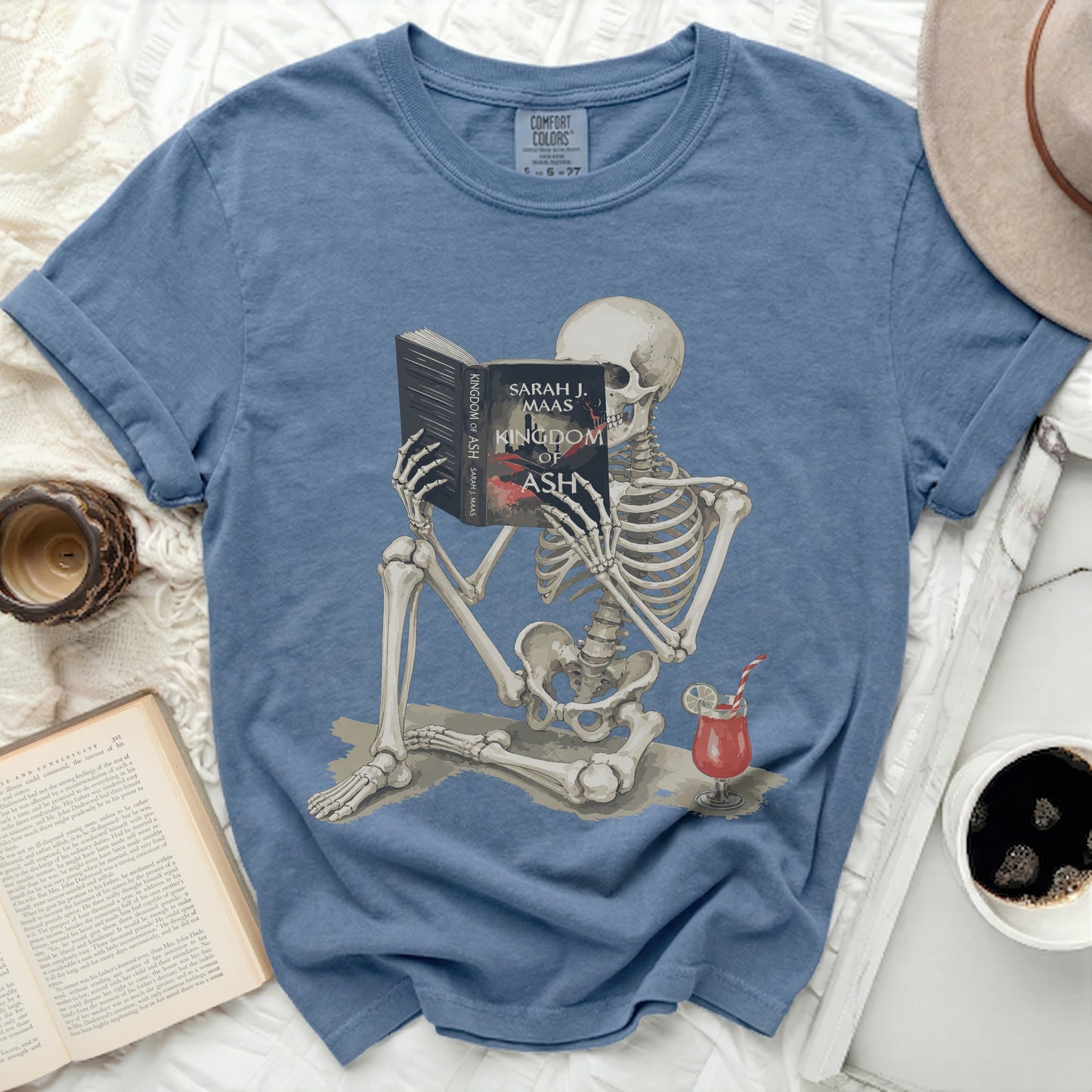 Skeleton reading "Kingdom of Ash" by Sarah J. Maas with a drink.