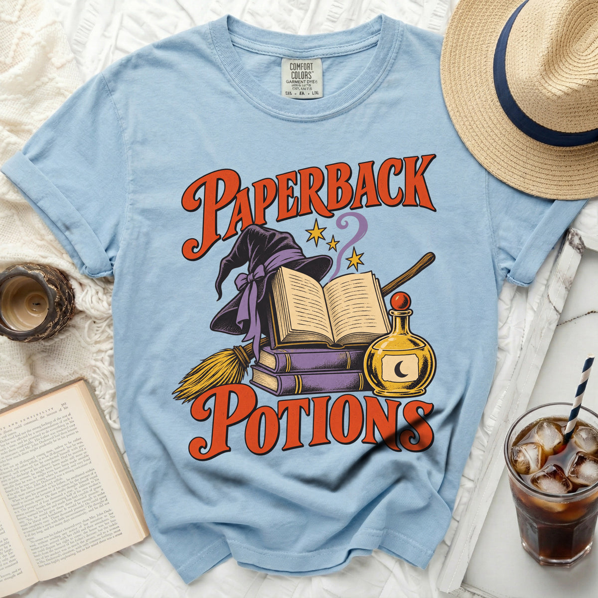 Light blue t-shirt with "Paperback Potions" graphic featuring books, hat, and potion bottle.