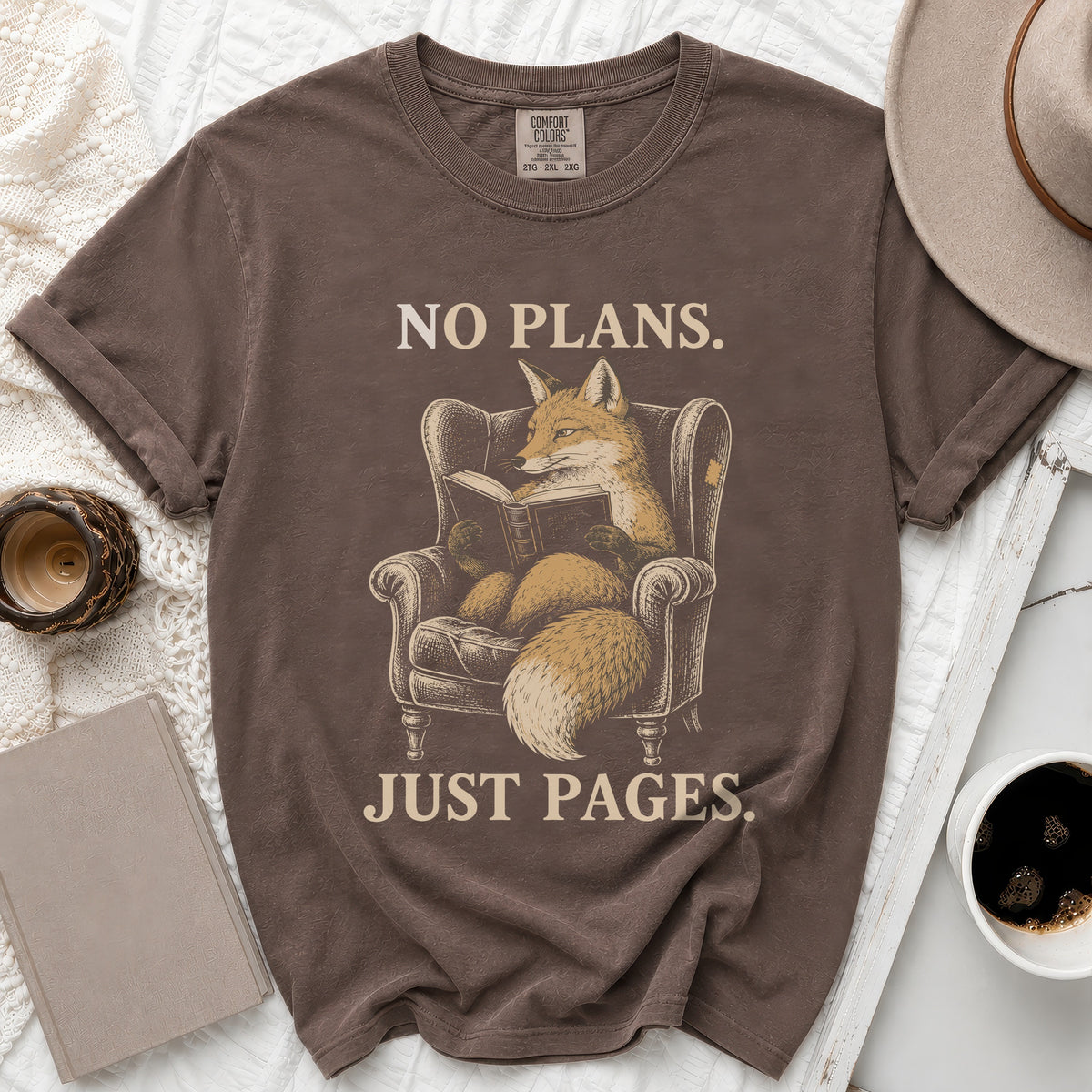 Brown t-shirt with graphic of fox reading a book and text "NO PLANS. JUST PAGES."