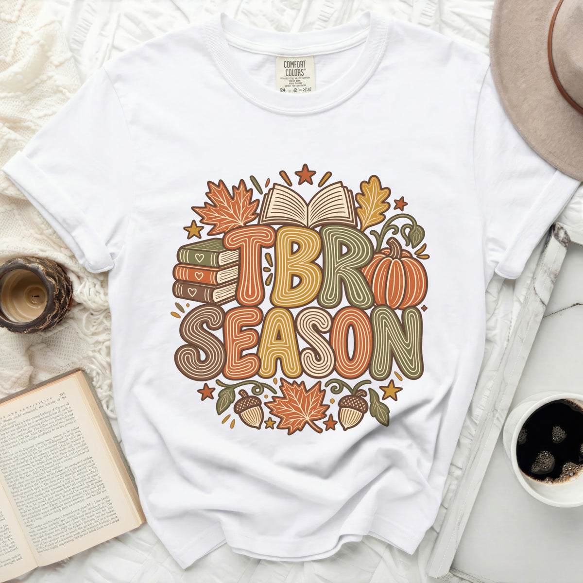 White t-shirt with "TBR SEASON" text surrounded by autumn leaves, books, and a pumpkin.