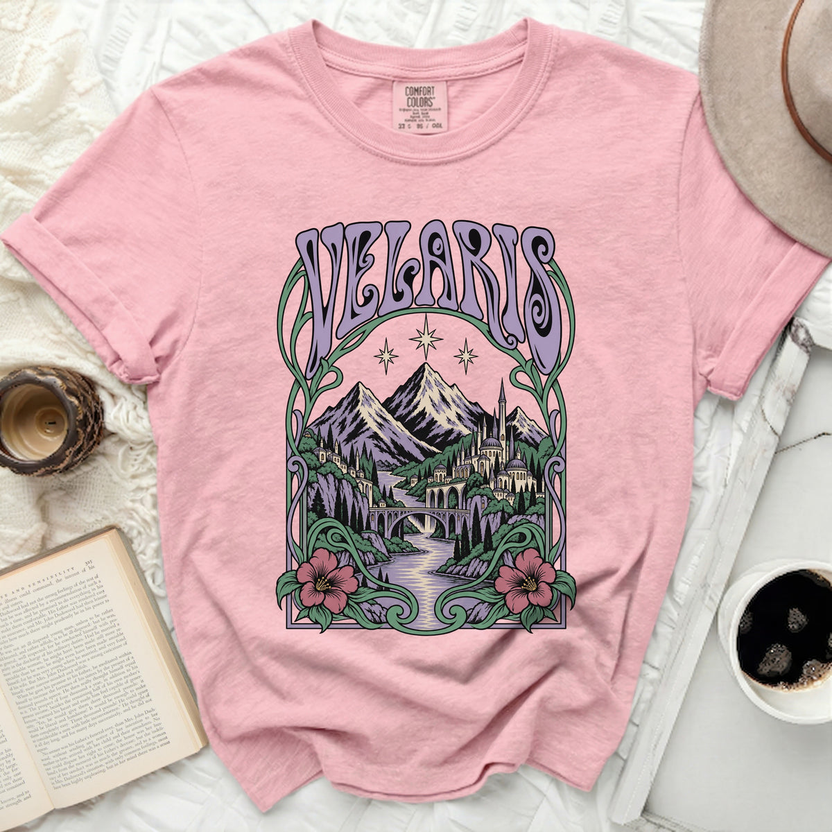 Pink t-shirt with "Velaris" in purple text above a scenic fantasy landscape.