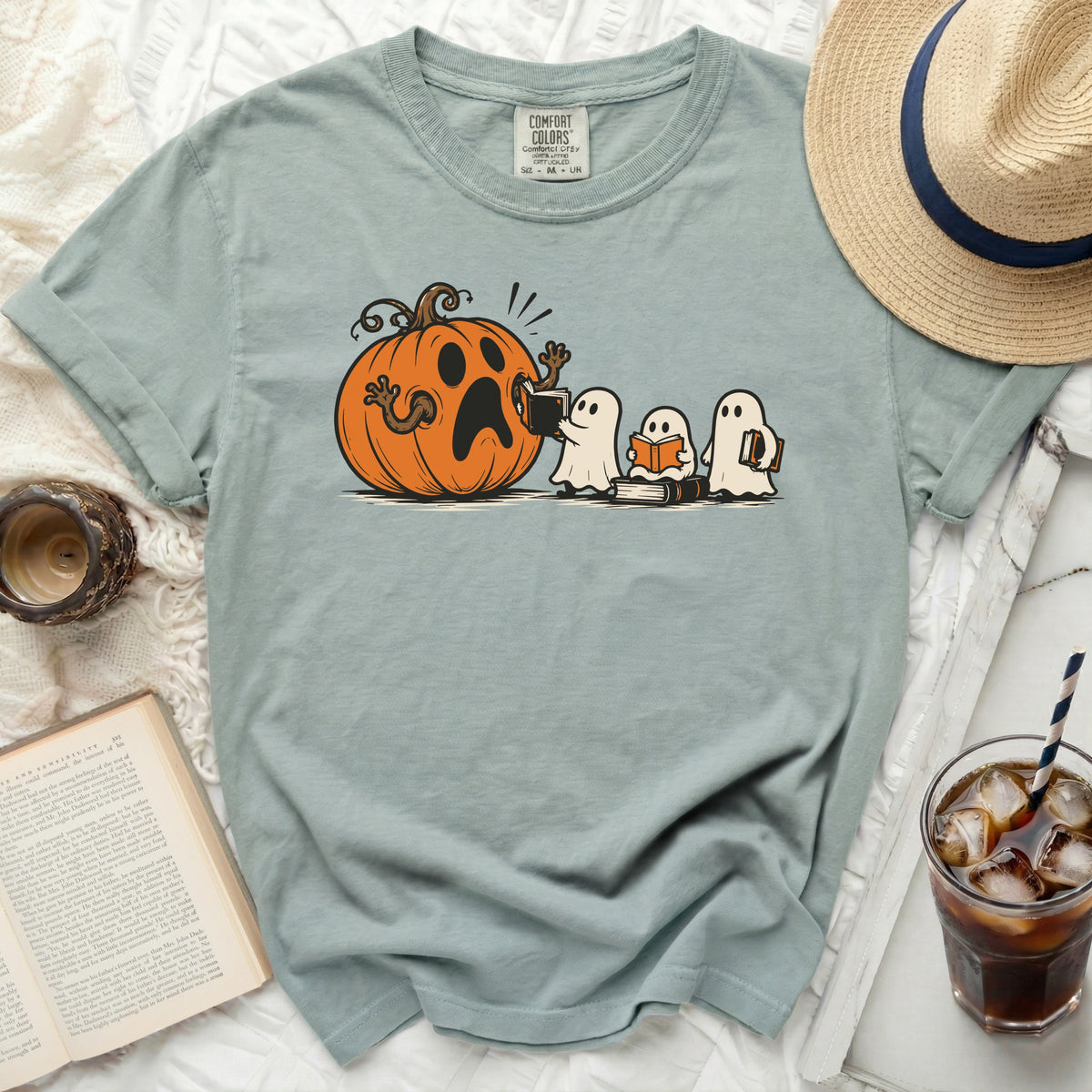 Ghost characters reading books beside a surprised pumpkin graphic on a light blue shirt.