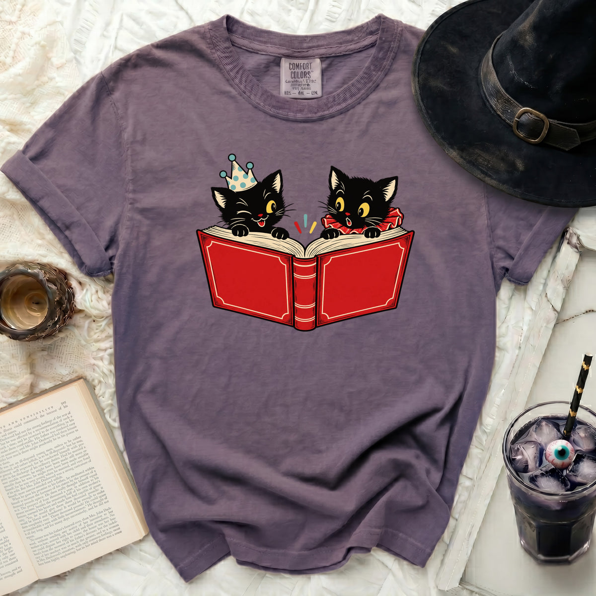 Two black kittens reading an open red book, one wearing a party hat.