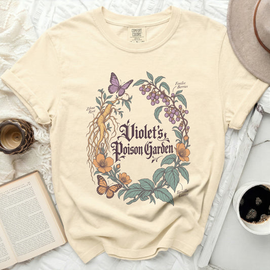 Cream t-shirt featuring a botanical illustration with text reading Violet’s Poison Garden, butterflies, and plants.