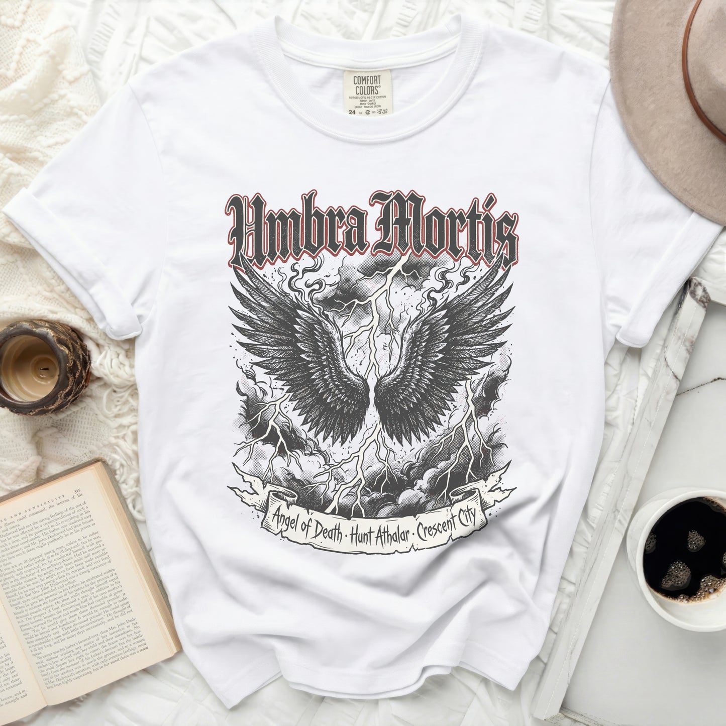 White t-shirt with "Umbra Mortis" and angel wings graphic.