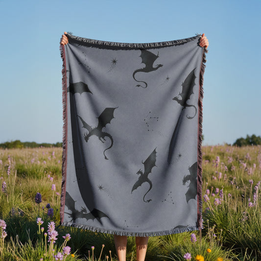 A person is holding up a gray blanket with black dragon silhouettes against a field of purple flowers.