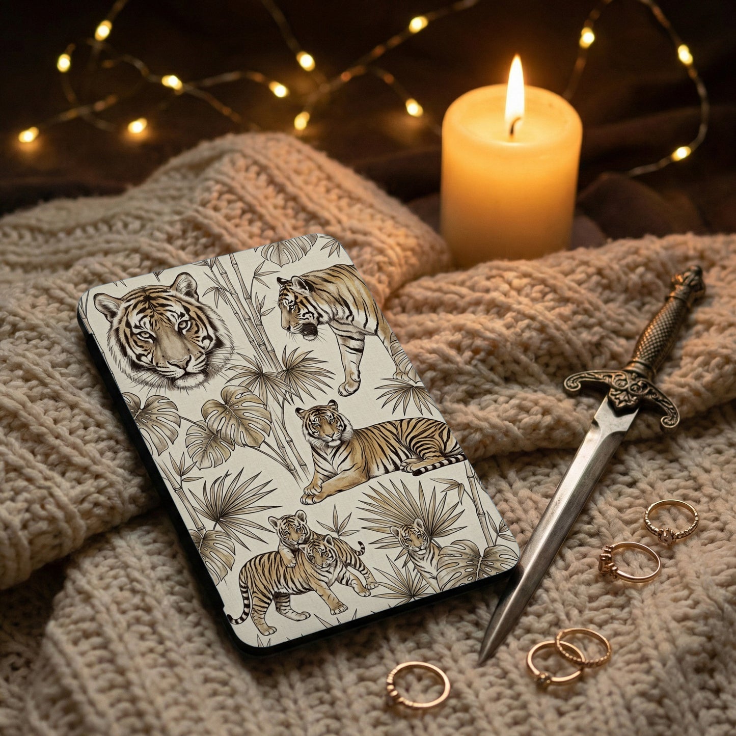 Patterned phone case with tigers, bamboo, and tropical leaves, next to a candle and rings.
