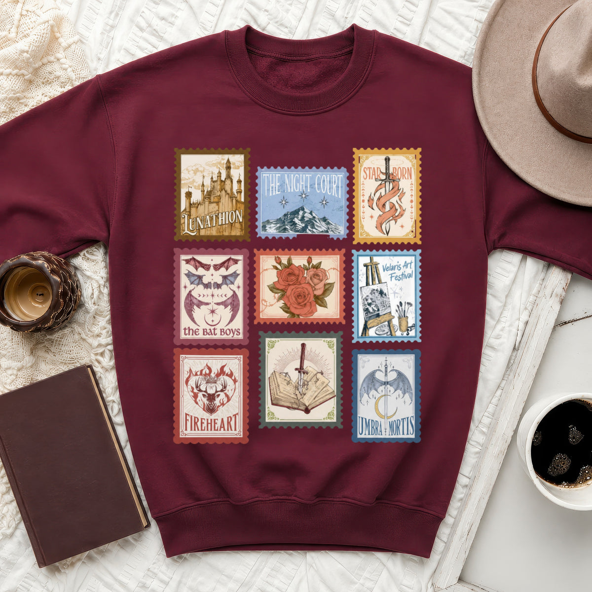 Maroon sweatshirt with nine postage stamp designs featuring fantasy elements and text.