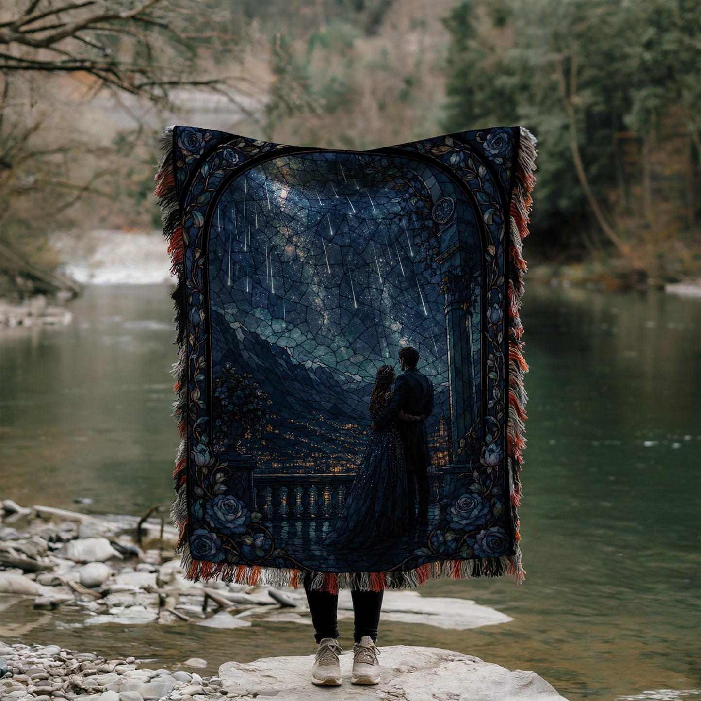 A person stands on a rock, holding a large, intricately designed quilt that features a nighttime scene with a couple embracing under a starry sky.