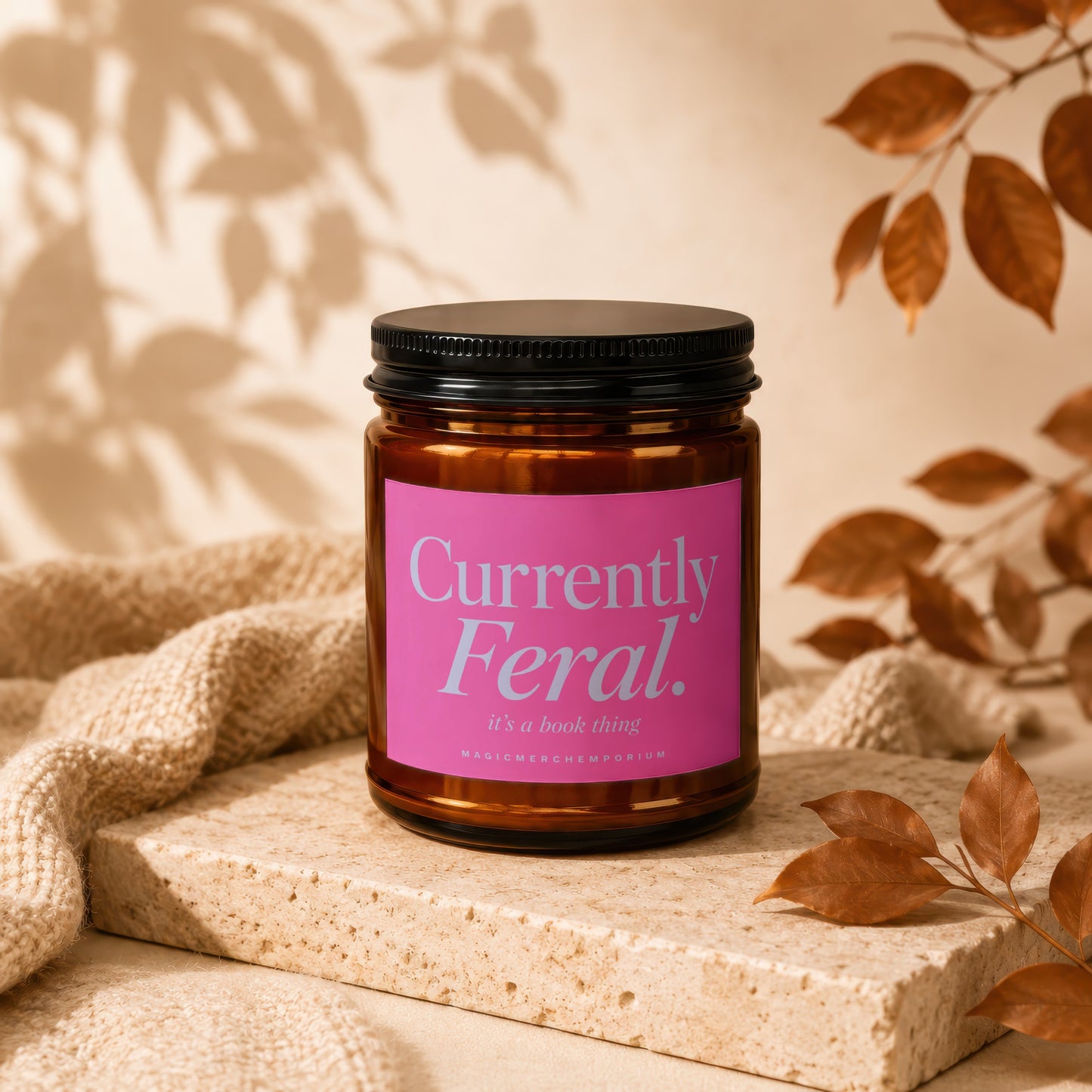 Amber jar candle with pink label reading "Currently Feral. it's a book thing."