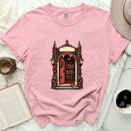 Pink t-shirt with gothic doorway graphic, vampire fangs, bookshelves, and cat eyes.