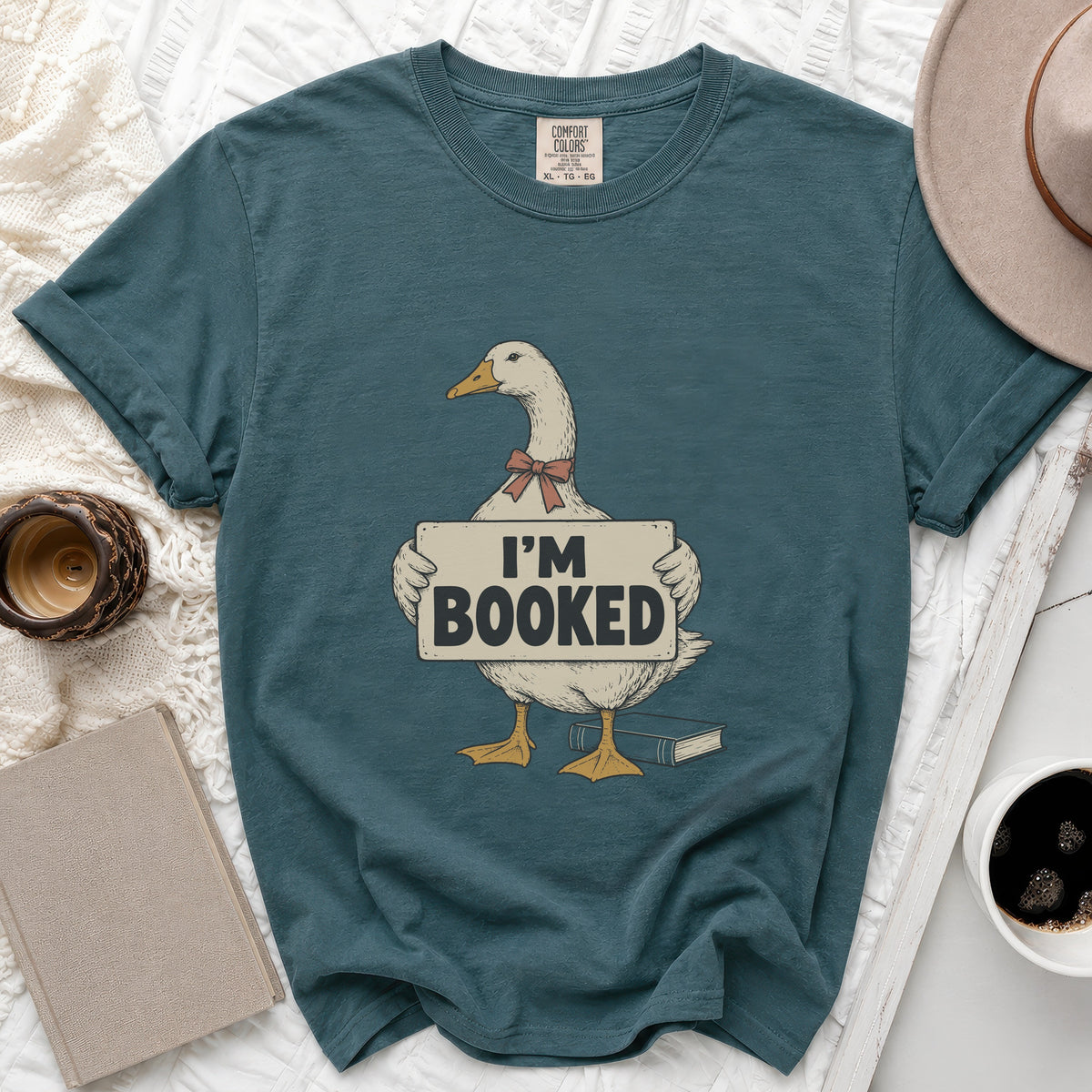 Goose wearing a bow tie holds a sign that says "I'M BOOKED" with a book nearby.