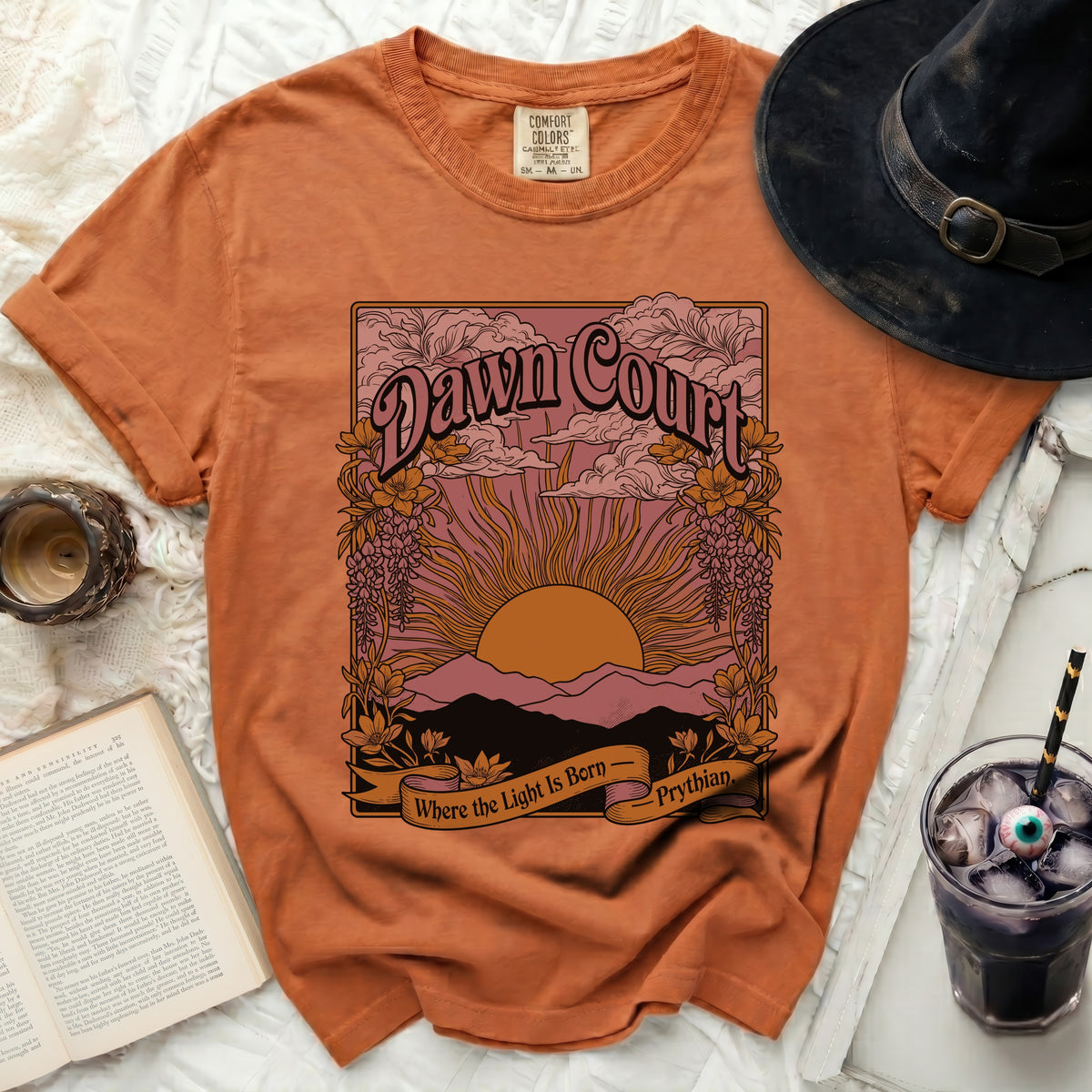 Orange t-shirt with "Dawn Court" graphic, sun, mountains, and floral details.