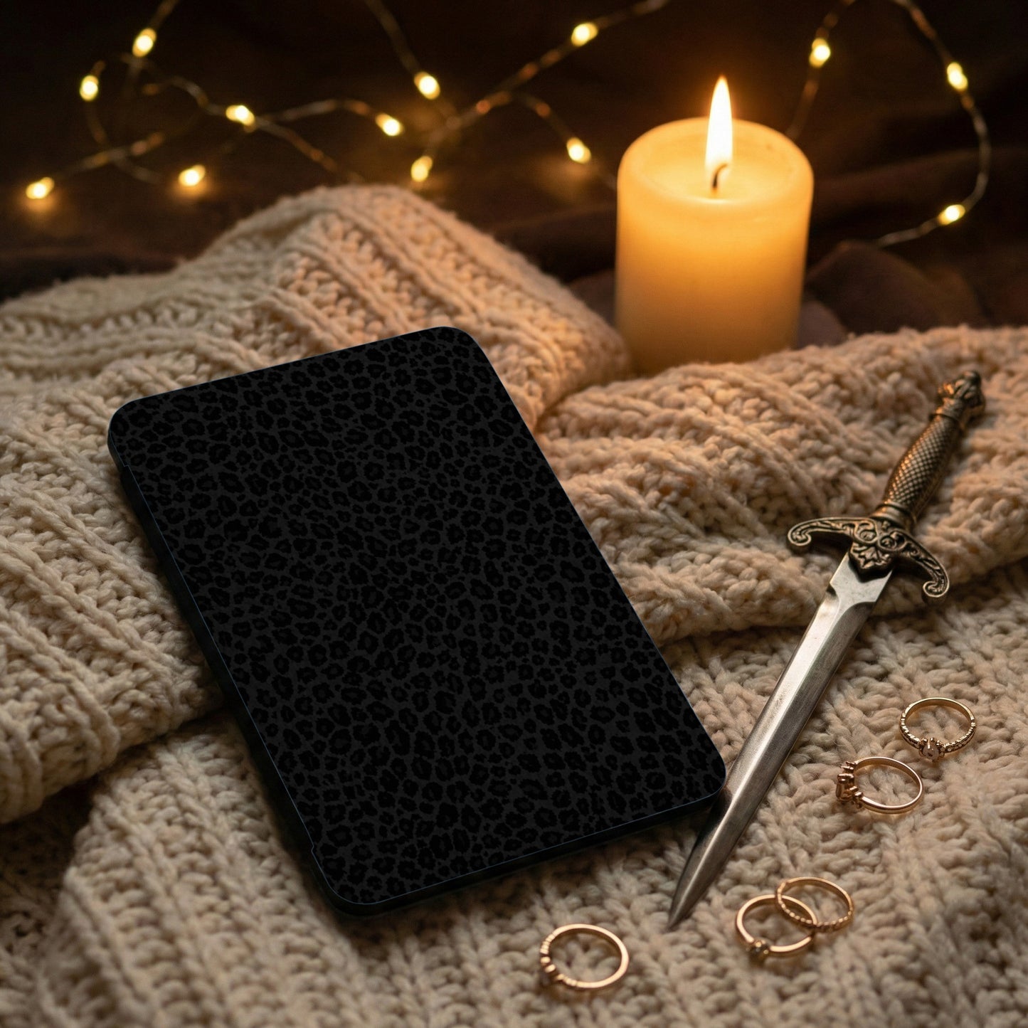 Black leopard print case on a knitted blanket with a sword and rings.