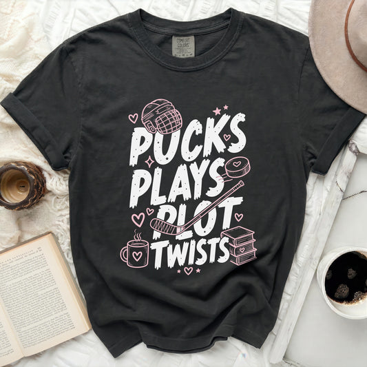 Black t-shirt with "Pucks Plays Plot Twists" in pink lettering and hockey graphics.