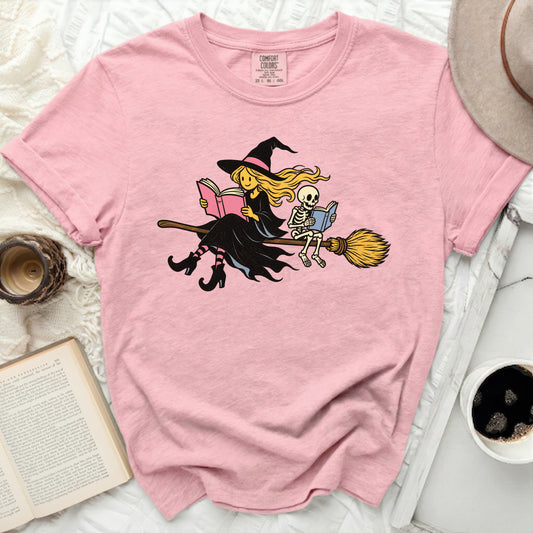 Pink t-shirt with witch and skeleton reading on broom graphic.