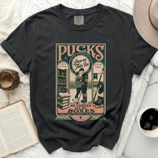 Black t-shirt with "Pucks, He Checks My Boxes" text and hockey couple illustration.