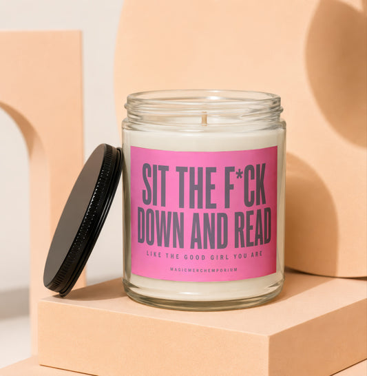 Glass candle with pink label that reads "SIT THE F*CK DOWN AND READ LIKE THE GOOD GIRL YOU ARE".