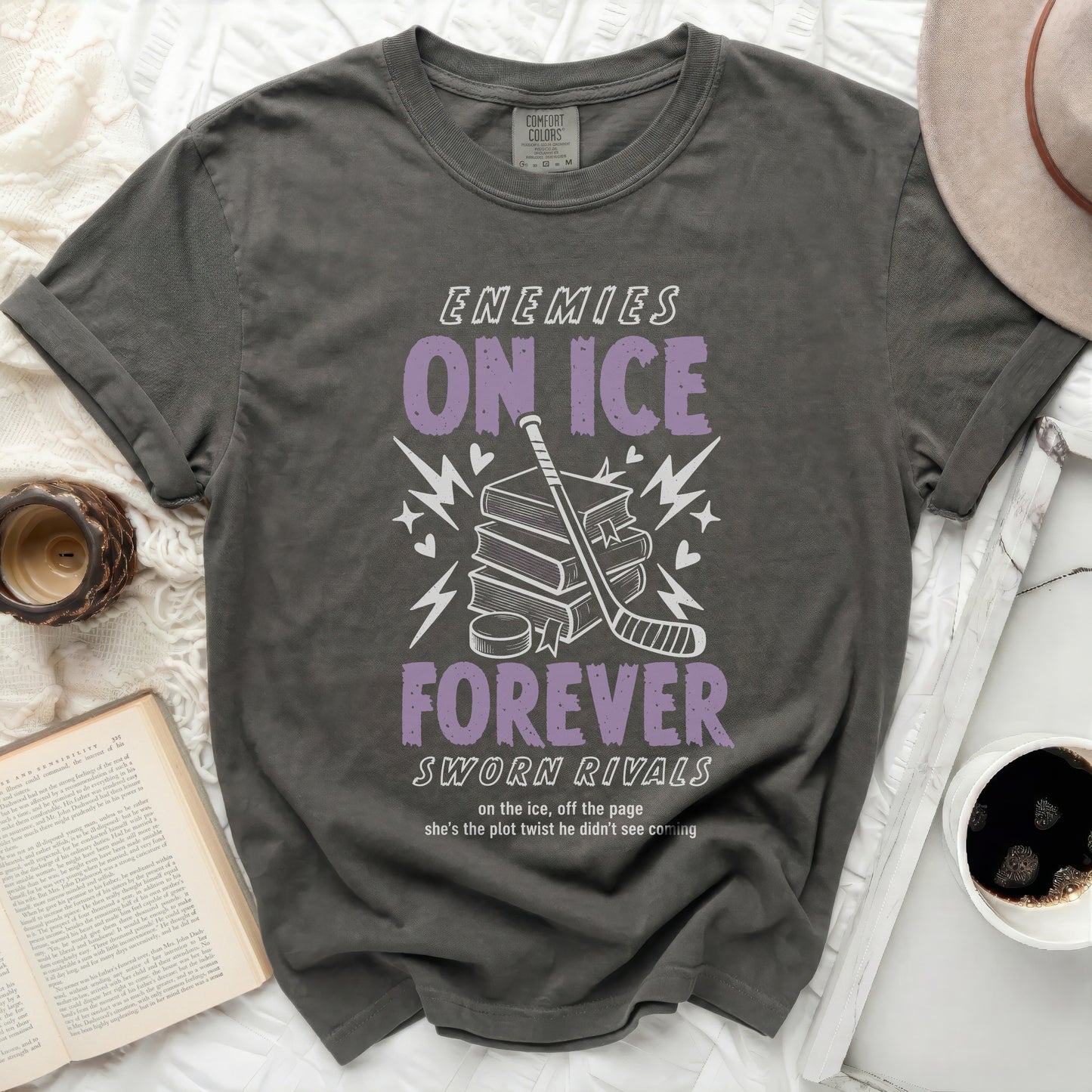 Dark grey t-shirt with "ENEMIES ON ICE SWORN RIVALS" text, hockey stick, and books.