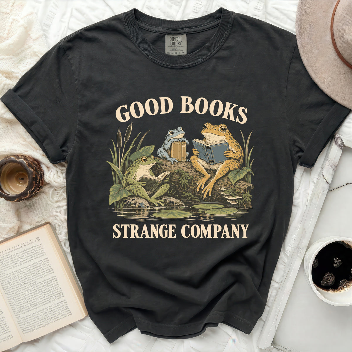 T-shirt with graphic of frogs reading books, "Good Books Strange Company" text.