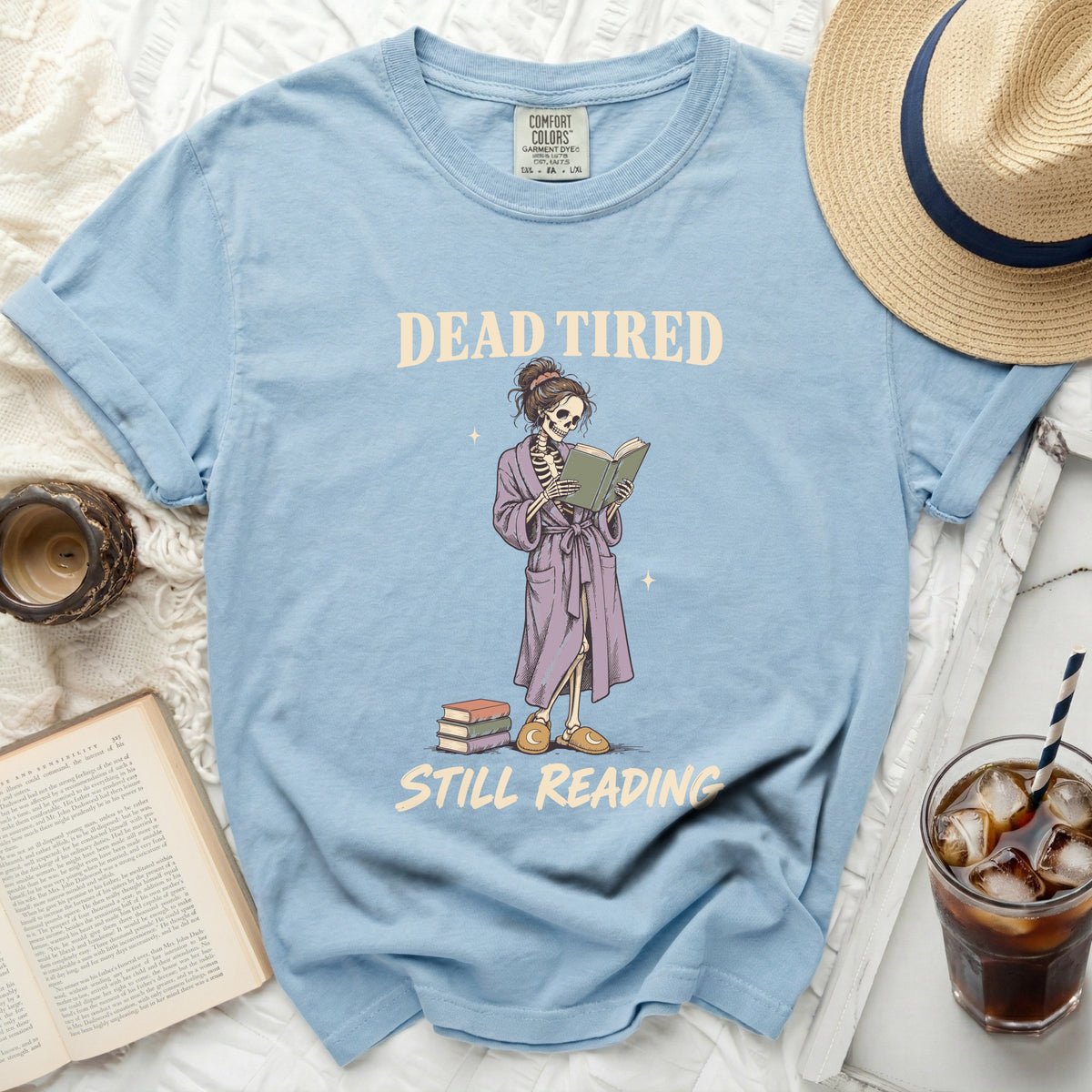 Light blue t-shirt with skeleton reading "Dead Tired Still Reading" graphic.