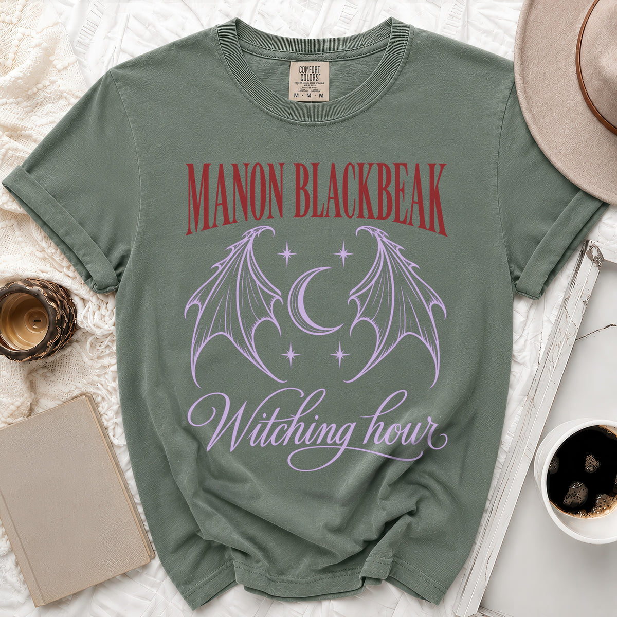 Sage green t-shirt with "MANON BLACKBEAK" and "Witching hour" text.