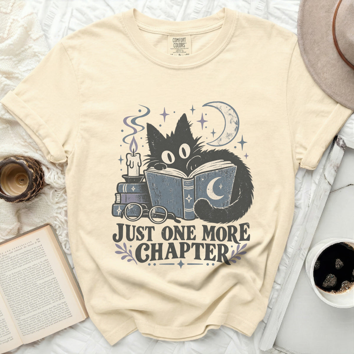 Cream t-shirt with black cat reading a book with text "JUST ONE MORE CHAPTER".