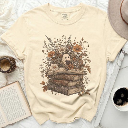 A ghost reading a book surrounded by vintage flowers and books on a cream t-shirt.