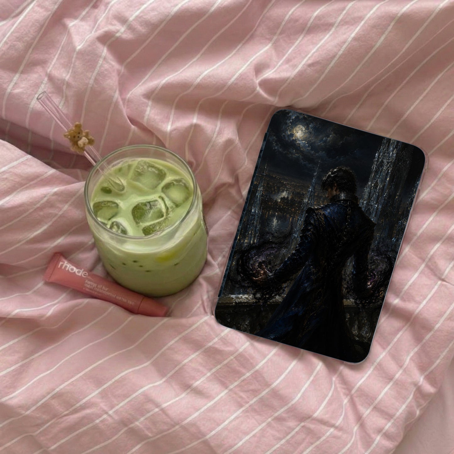 Glass of matcha with ice,RHODE lip balm, and a phone case with artwork.
