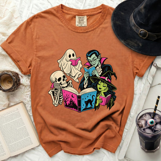 Orange t-shirt with skeleton, ghost, vampire, and witch reading books.