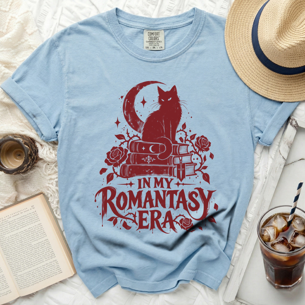 Light blue t-shirt with red graphic of a cat on books, crescent moon, and roses with text.