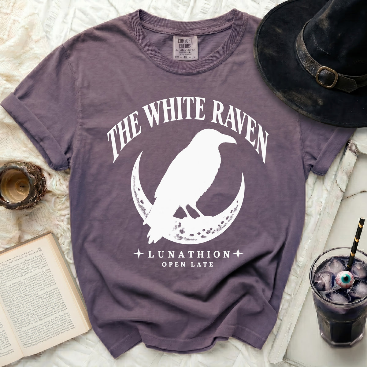 Purple t-shirt with white graphic of a raven on a crescent moon and text.