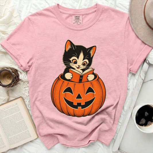 Pink t-shirt with a graphic of a kitten reading a book in a jack-o'-lantern.