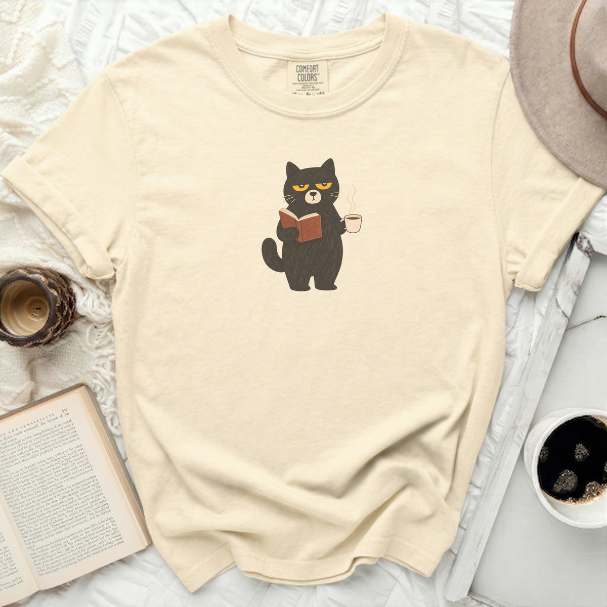 Black cat wearing glasses, reading a book and holding coffee.