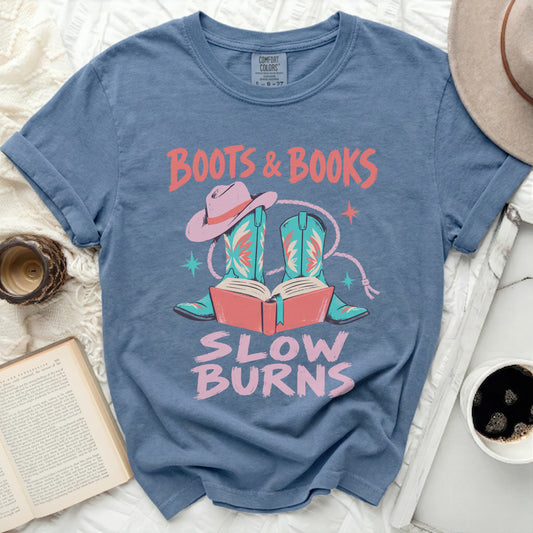 Blue t-shirt with "Boots & Books Slow Burns" graphic featuring boots, a hat, and books.