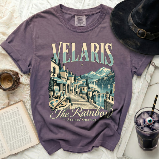 Purple t-shirt with "Velaris The Rainbow Artists' Quarter" graphic depicting a scenic town.