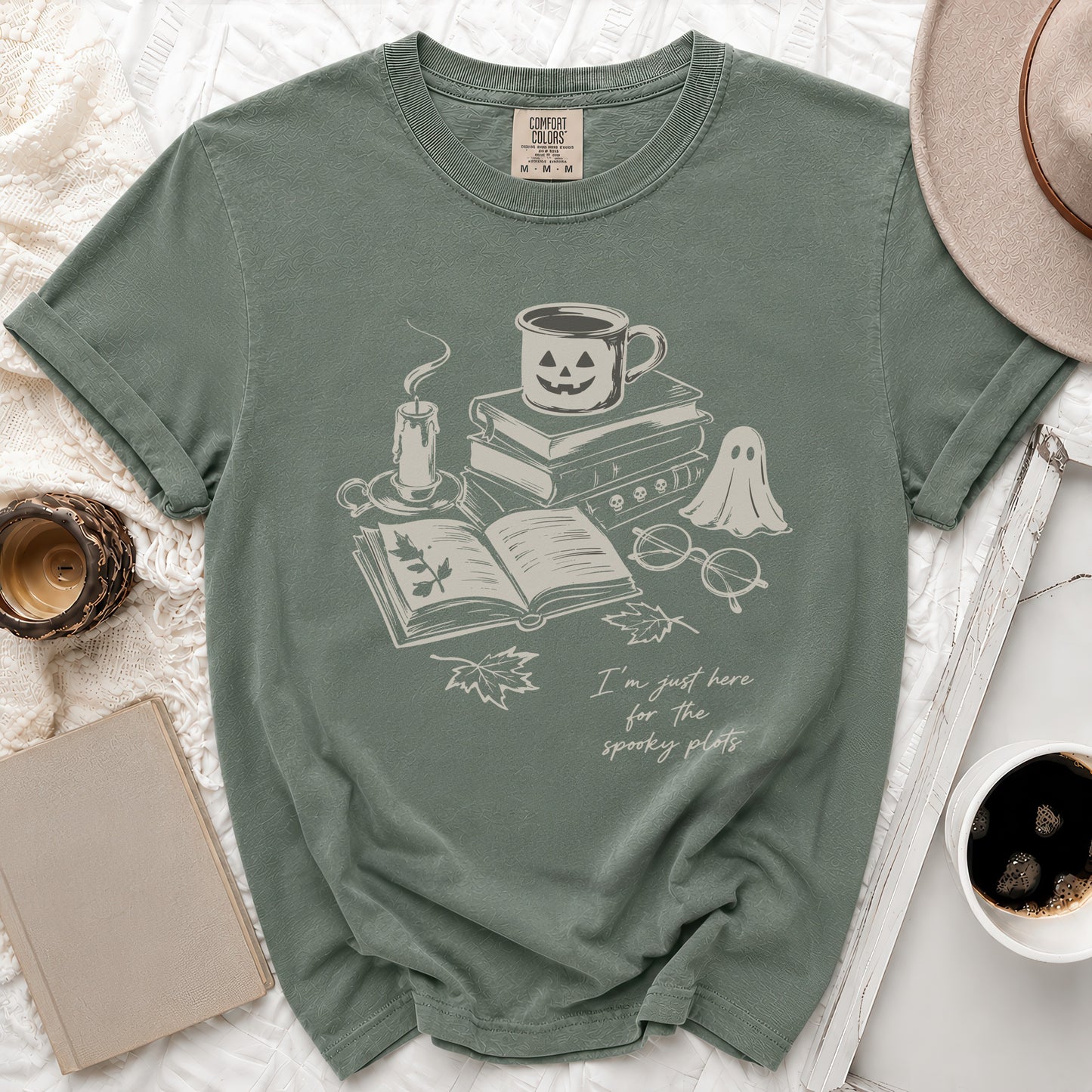 Green t-shirt with spooky plots graphic: candle, books, pumpkin mug, ghost, and text.