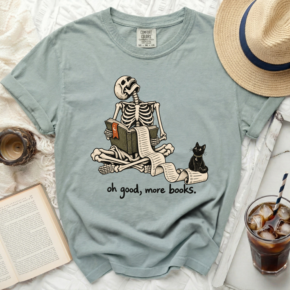 Skeleton reading book with checklist and cat, "oh good, more books." text.