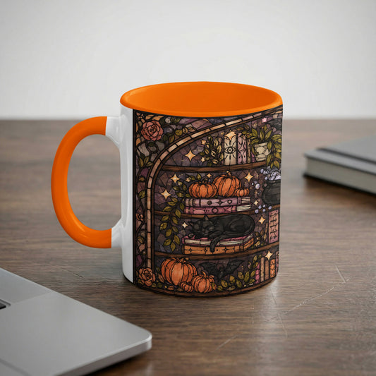 A white mug with an orange handle features a stained-glass design of a cat, pumpkins, and bats.