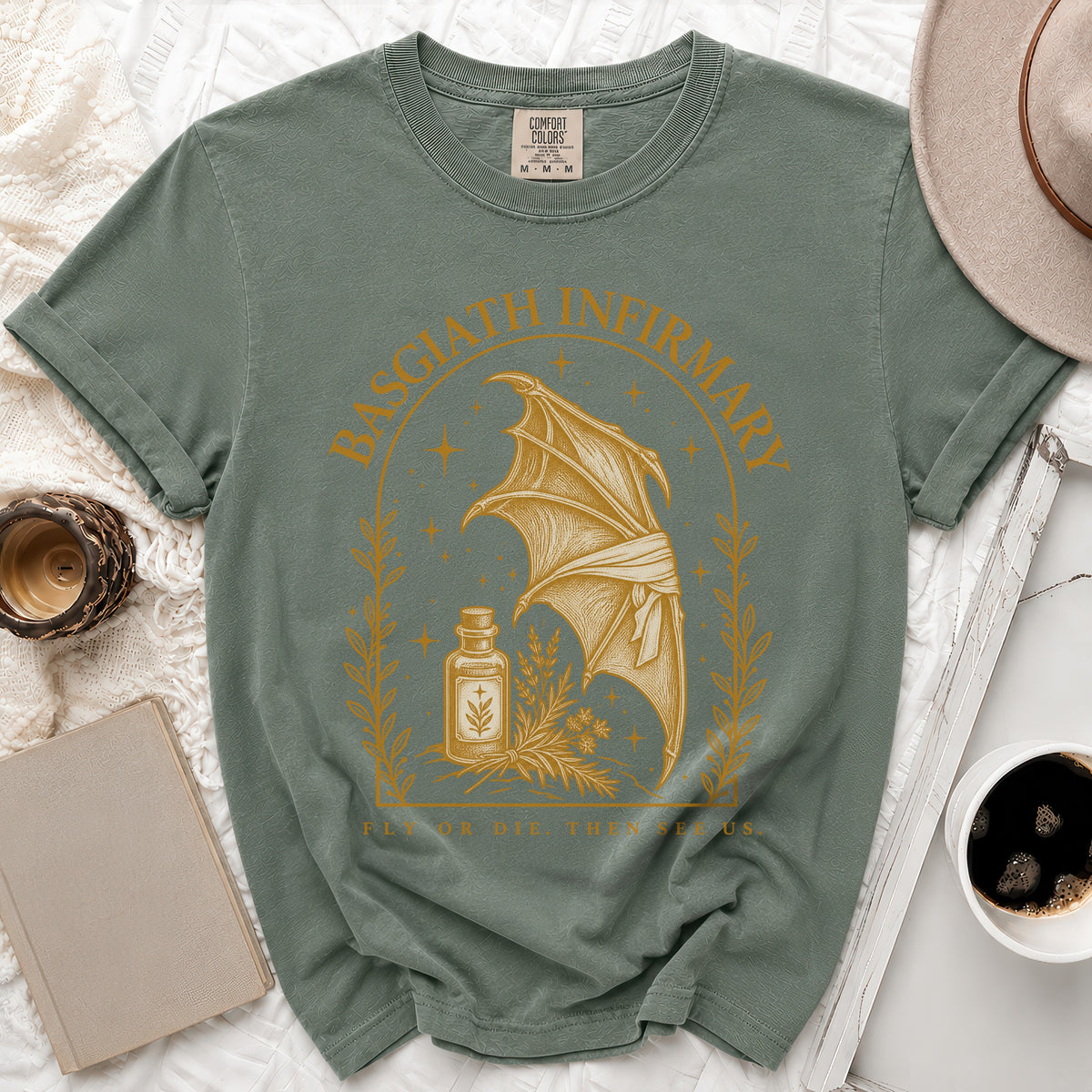 Sage green t-shirt featuring a gold graphic of a dragon wing, potion bottle, and Basgiath Infirmary text.