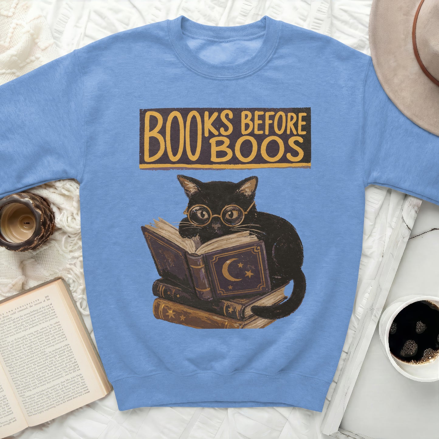Light blue sweatshirt graphic of black cat reading books with "Books Before Boos" text.
