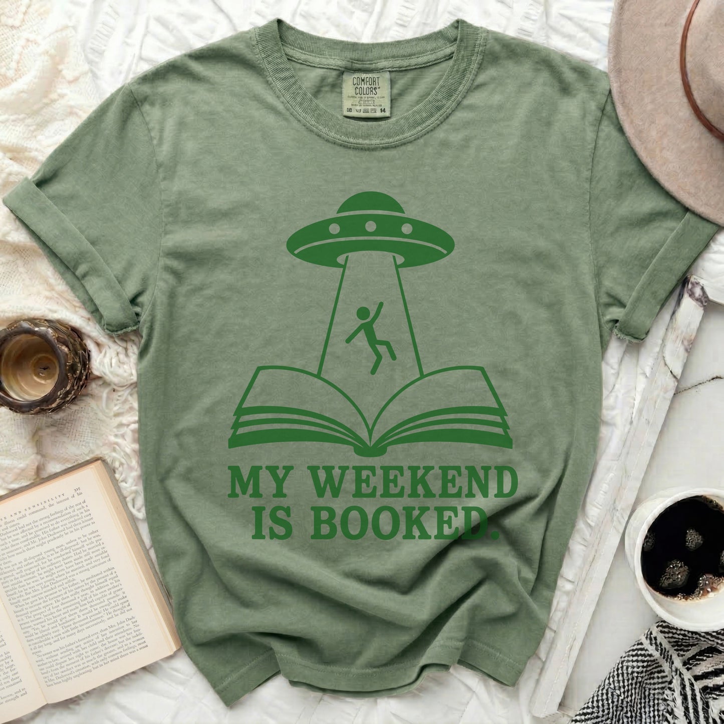 Green t-shirt with UFO abducting a person from an open book.
