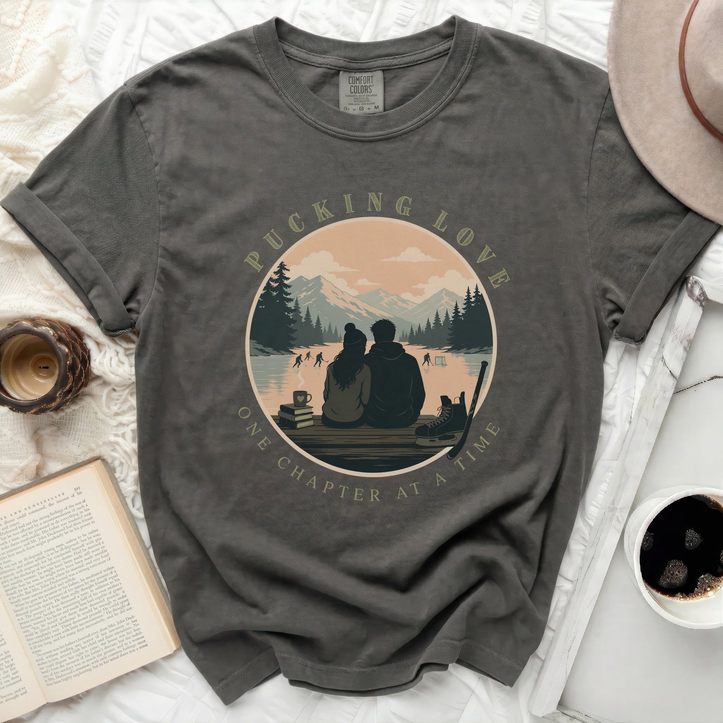 Dark grey t-shirt with circular graphic of couple ice skating, text "PUCKING LOVE ONE CHAPTER AT A TIME".