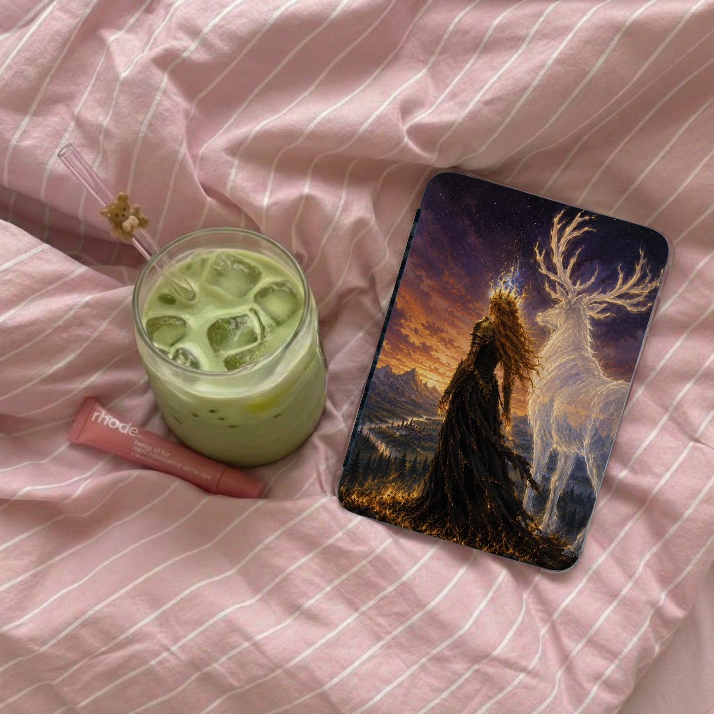 Phone case with queen and stag artwork on pink striped bedding with matcha drink and lip balm.