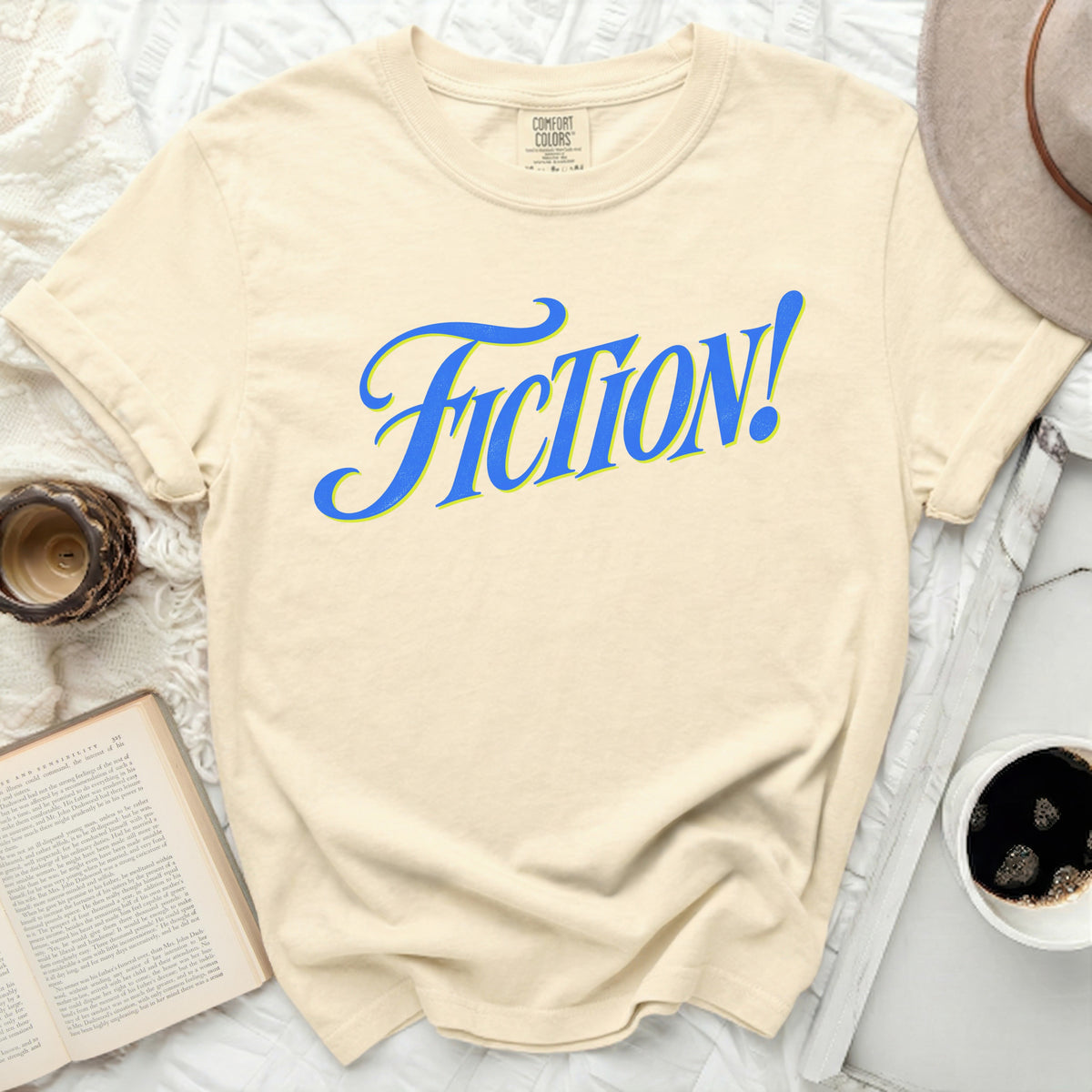 Cream Comfort Colors t-shirt with "FICTION!" in blue and yellow script.