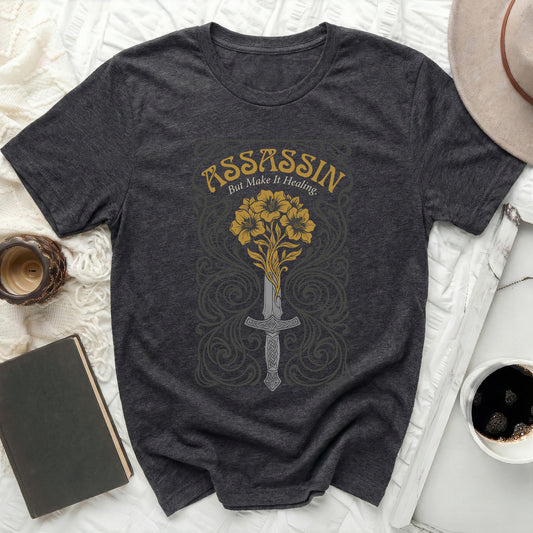 Dark grey t-shirt with sword and flowers design, text "ASSASSIN BUT MAKE IT HEALING."