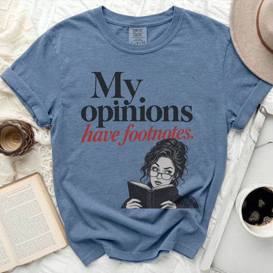Blue t-shirt with black text "My opinions have footnotes" and a drawing of a woman reading.