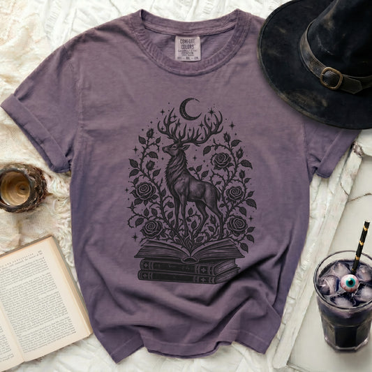Faded purple t-shirt featuring a black graphic of a stag emerging from books, surrounded by roses and a crescent moon.
