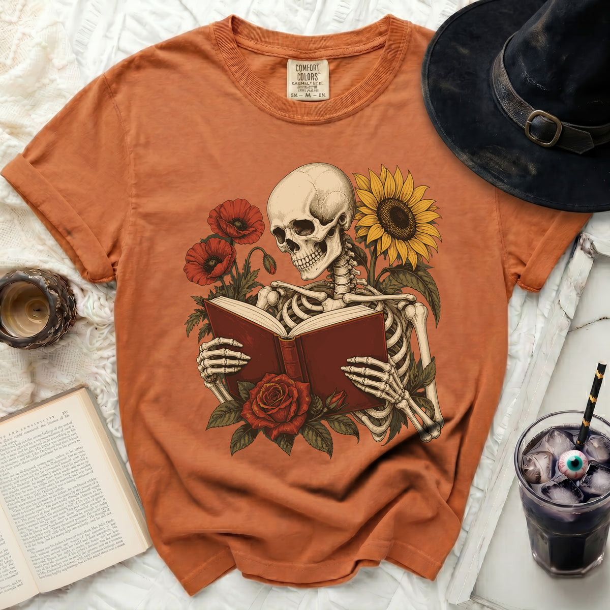 Skeleton reading a book surrounded by poppies and a sunflower on an orange t-shirt.